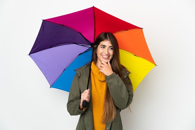 Jeune femme tenant un parapluie isolé sur fond blanc regardant sur le côté et souriant