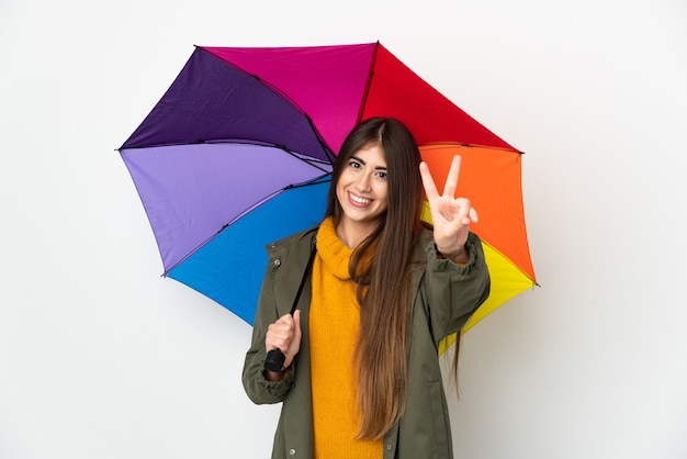 Jeune femme tenant un parapluie isolé sur fond blanc souriant et montrant le signe de la victoire