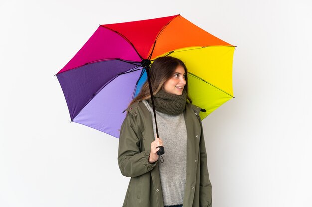 Jeune femme tenant un parapluie isolé sur un mur blanc à côté