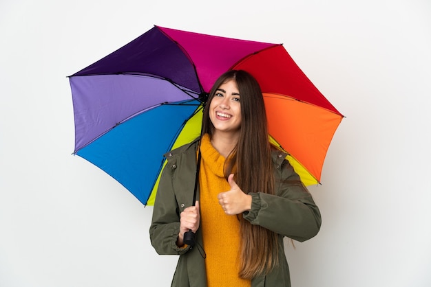 Jeune femme tenant un parapluie isolé sur un mur blanc donnant un geste de pouce en l'air