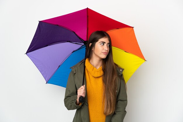 Jeune femme tenant un parapluie isolé sur un mur blanc à la recherche sur le côté