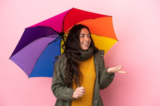 Jeune femme tenant un parapluie isolé sur un mur rose avec une expression de surprise tout en regardant côté