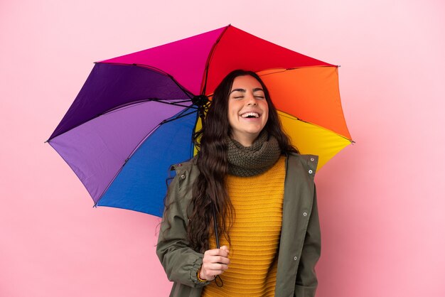 Jeune femme tenant un parapluie isolé sur un mur rose en riant