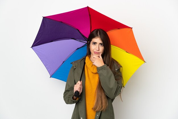 Jeune femme tenant un parapluie isolé sur la pensée de mur blanc