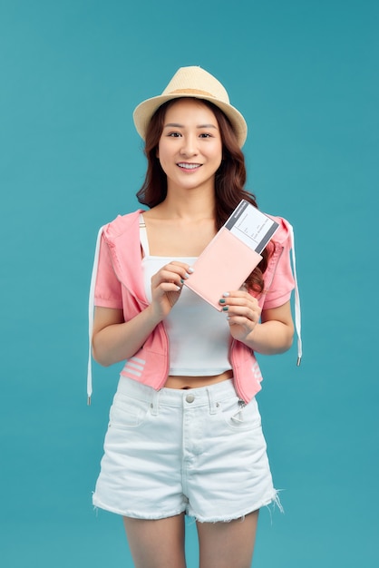 Jeune femme tenant un passeport, carte de crédit. Voyageur de fille souriante sur fond bleu.