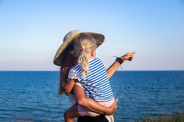 Jeune femme tenant une petite fille dans ses bras pointant du doigt la mer.