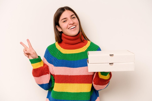 Jeune femme tenant des pizzas isolées sur fond blanc joyeuse et insouciante montrant un symbole de paix avec les doigts