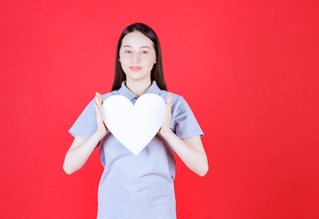 Jeune femme tenant une planche en forme de coeur et regardant à l'avant