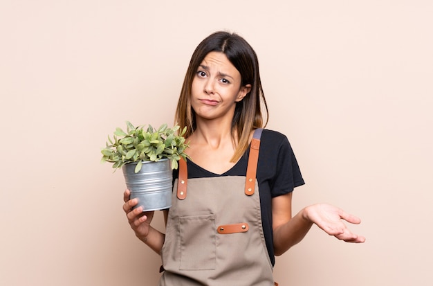 Jeune femme tenant une plante faisant un geste de doute tout en soulevant les épaules