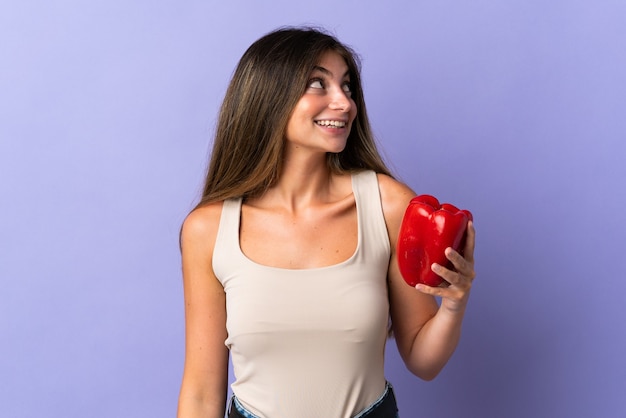 Jeune femme tenant un poivron isolé sur violet en levant en souriant