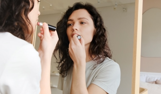 Jeune femme tenant le rouge à lèvres dans ses mains et peint ses lèvres se prépare à se préparer le matin. Femme maquillant. Préparez-vous pour une date.