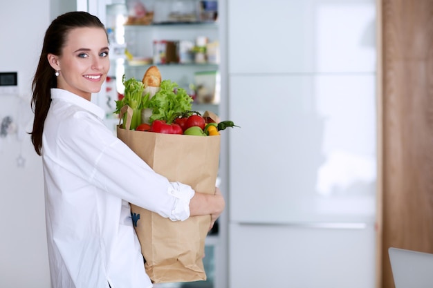 Jeune femme tenant un sac d'épicerie avec des légumes Debout dans la cuisine Femme dans la cuisine en regardant la caméra