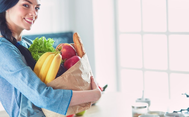 Jeune femme tenant un sac d'épicerie avec des légumes debout dans la cuisine