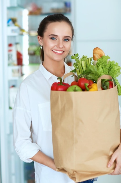 Jeune femme tenant un sac d'épicerie avec des légumes debout dans la cuisine