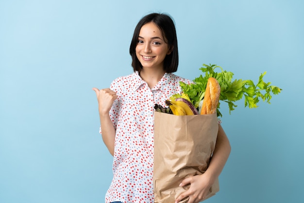 Jeune femme tenant un sac d'épicerie pointant vers le côté pour présenter un produit