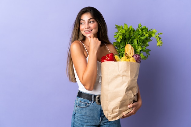 Jeune femme tenant un sac d'épicerie à la recherche sur le côté et souriant