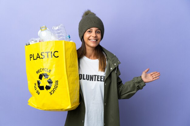 Jeune femme tenant un sac plein de plastique s'étendant les mains sur le côté pour inviter à venir