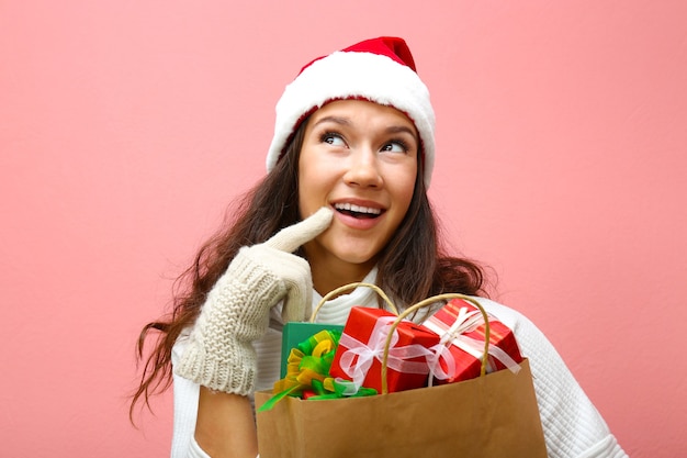 Jeune femme tenant un sac à provisions avec des cadeaux de Noël sur fond rose