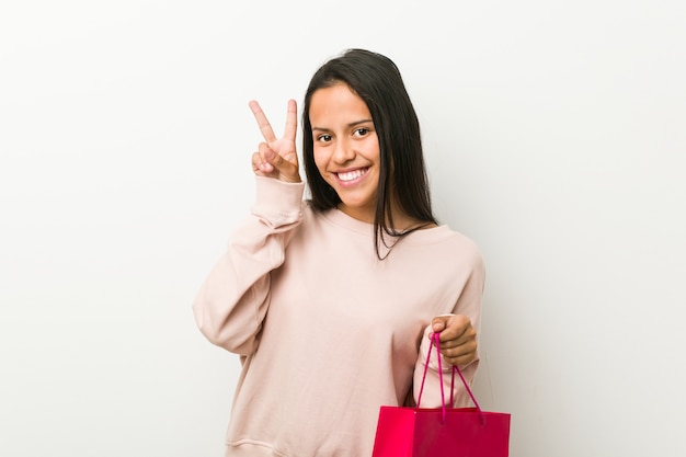 Jeune femme tenant un sac à provisions montrant le signe de la victoire et souriant largement.