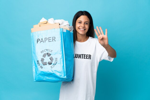 Jeune femme tenant un sac de recyclage plein de papier heureux et comptant quatre avec les doigts