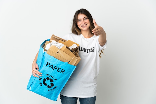 Jeune femme tenant un sac de recyclage plein de papier à recycler isolé sur blanc se serrant la main pour conclure une bonne affaire