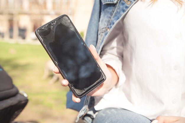 Jeune femme tenant un smartphone cassé à l'extérieur.