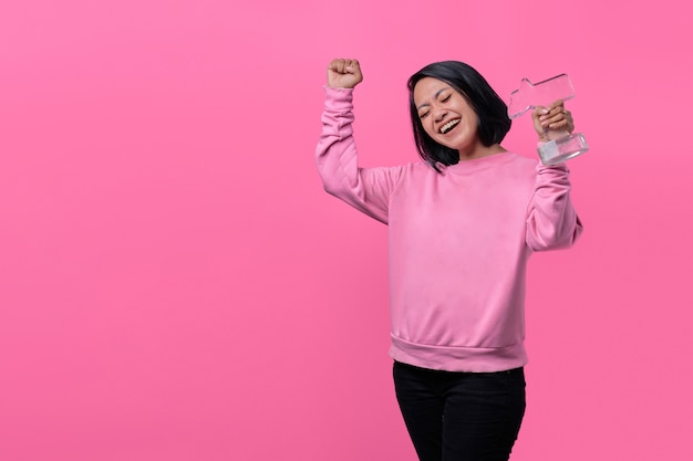 Jeune femme tenant une statuette de prix recevant une agréable surprise, excitée et levant les mains