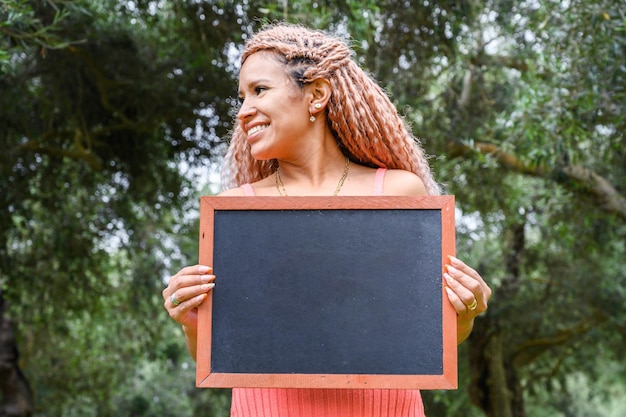 Photo une jeune femme tenant un tableau noir contre des arbres