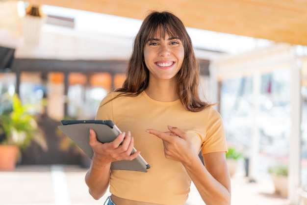 Jeune femme tenant une tablette à l'extérieur et la pointant