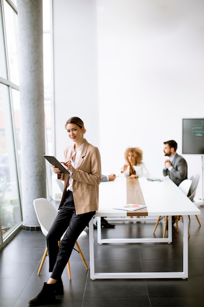 Jeune femme tenant une tablette numérique et travaillant dans un bureau moderne devant son équipe