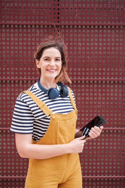 Jeune femme tenant une tablette vêtue d'une salopette jaune sur fond rouge Style de mode de vie Concept à l'extérieur