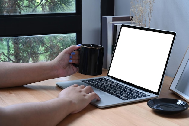 Jeune femme tenant une tasse de café et utilisant un ordinateur portable à la maison.