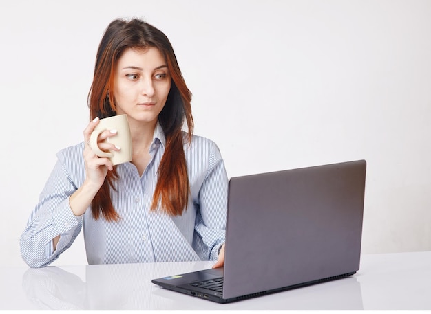 Jeune femme tenant une tasse et travaillant avec un ordinateur