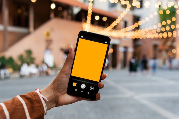 Jeune femme tenant un téléphone portable pour prendre des photos dans la ville.