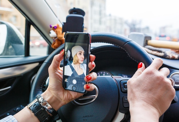 Jeune femme tenant un téléphone portable et prenant des photos en conduisant une voiture