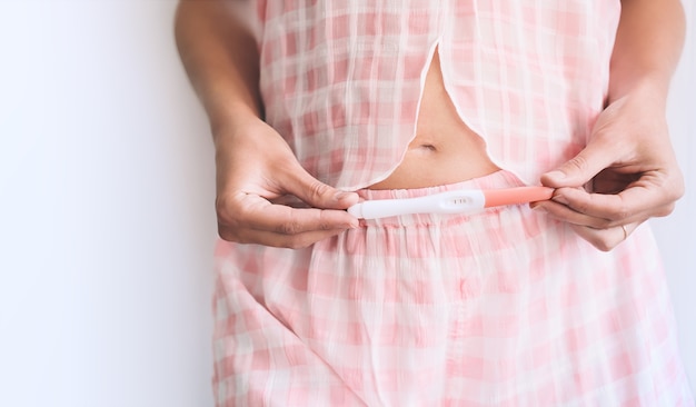 Jeune femme tenant un test de grossesse dans les mains et serrant son ventre