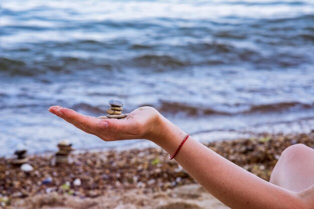 Jeune femme tenant une tourelle de galets de mer dans la main sur fond flou avec des vagues de la mer.