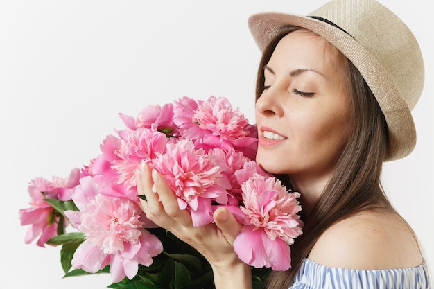 Jeune femme tendre en robe bleue, chapeau tenant, reniflant bouquet de fleurs de pivoines roses isolées sur fond blanc. Saint-Valentin, concept de vacances de la Journée internationale de la femme. Espace publicitaire.