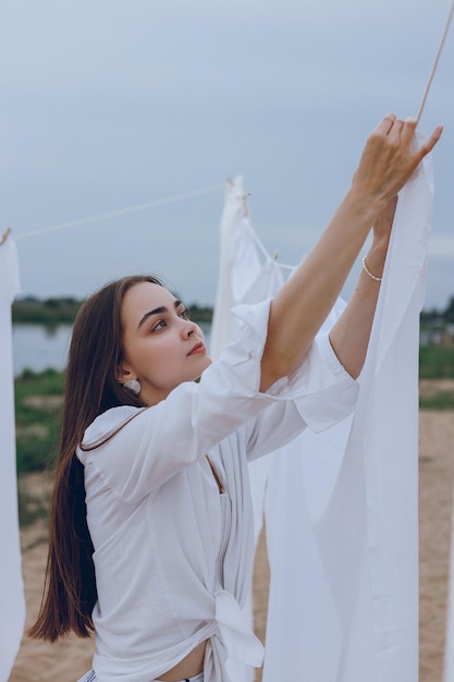 Jeune femme tendre en vêtements de lin blanc étendre le linge à l'extérieur en été