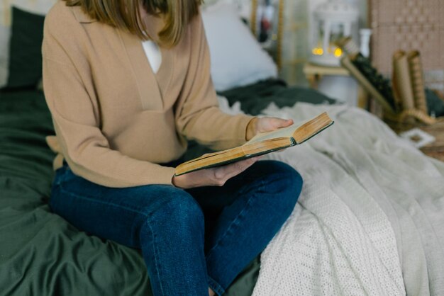 Jeune femme en tenue décontractée lisant un livre tout en se relaxant sur le lit à la maison pendant les vacances de Noël