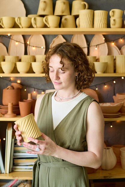 Jeune femme en tenue décontractée regardant une tasse d'argile faite à la main dans ses mains