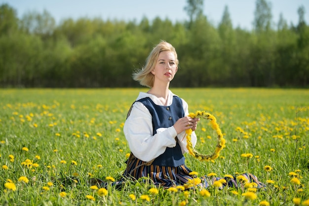 Jeune femme en tenue nationale portant une couronne de pissenlit jaune dans le champ de printemps