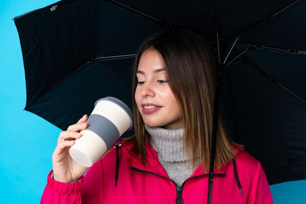 Jeune, femme, tenue, parapluie, café, emporter, isolé, bleu, mur