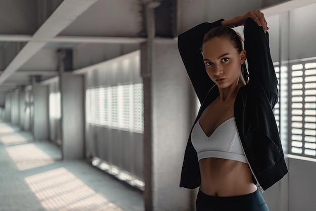 Une jeune femme en tenue sportive fait des exercices d'échauffement près du stade. Étirement des mains