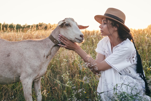 Jeune femme sur le terrain se promène avec des chèvres La fille et les chèvres dans le pré en été Amour pour les animaux Ferme de chèvre Animaux de compagnie Femme heureuse avec animal Gentillesse et amour pour les animaux Embrasse un animal de compagnie