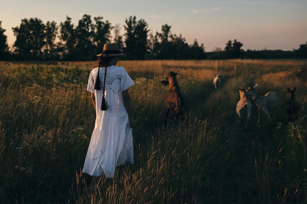 Jeune femme sur le terrain se promène avec des chèvres La fille et les chèvres dans le pré en été Amour pour les animaux Ferme de chèvre Animaux de compagnie Femme heureuse avec animal Gentillesse et amour pour les animaux