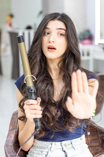 Jeune femme terrifiée assise sur une chaise au salon de coiffure et geste d'arrêt Photo de haute qualité