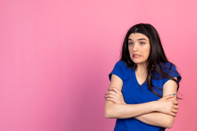 Une jeune femme terrifiée croisa la main et regarda de côté le fond rose Photo de haute qualité