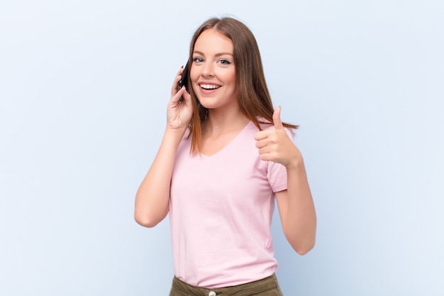 Jeune femme tête rouge contre un mur plat avec un téléphone intelligent