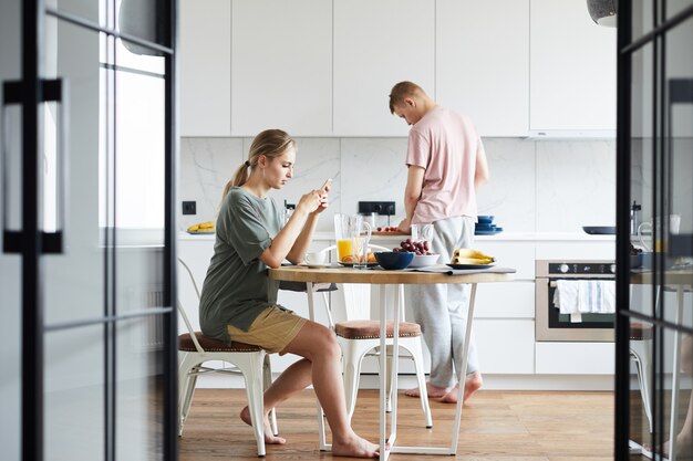 Jeune femme textos dans smartphone pendant que son mari cuisine